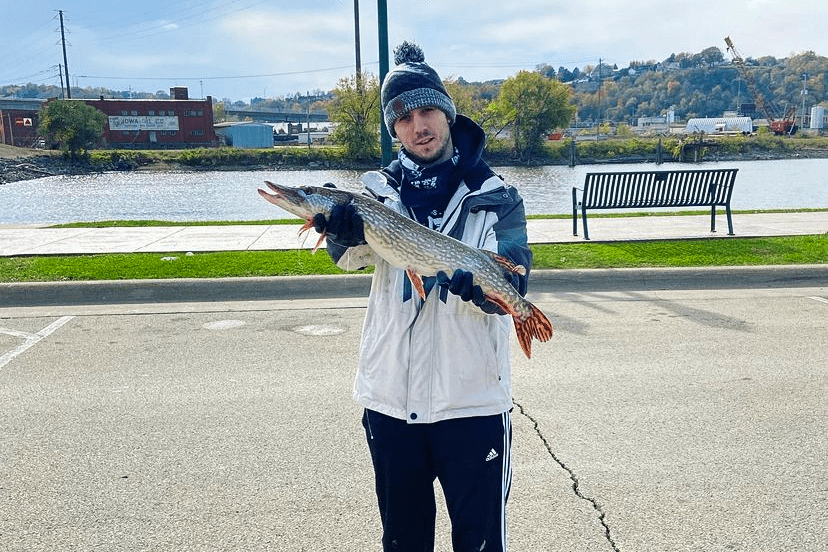man holds fish in front of river